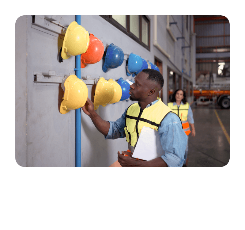 A man in a safety vest and hard hat examines a wall displaying various hats, showcasing his interest in headgear.